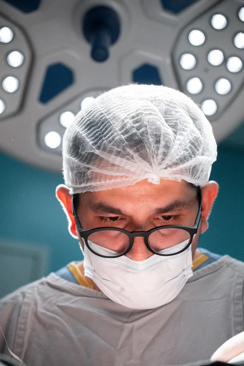 Dr. John Terrazas no centro cirúrgico, de touca e máscara